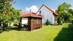 Ein Haus mit rotem Dach, weißer Fassade und einer kleinen Holzkonstruktion mit Bank und Stühlen davor.