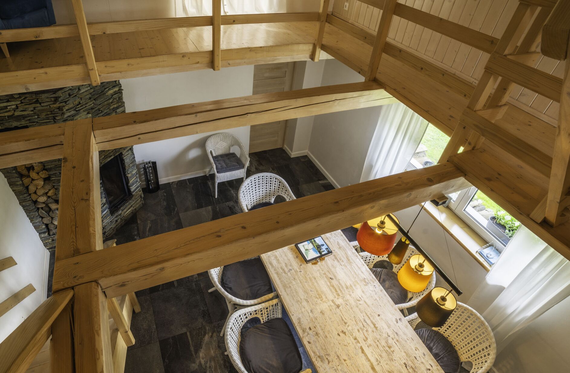 Interior em madeira com teto alto, sala de jantar com mobiliário de vime e vista para o exterior.