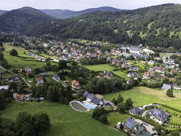 An aerial view of a residential area with houses, green fields, and a small pond.