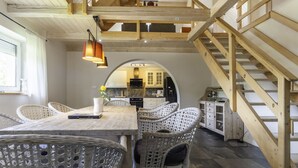 A dining area with a wooden table and wicker chairs, a staircase, and an arched doorway leading to a kitchen. - Willa Sonia by Interhome (Zawoja)