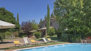 Una piscina con sillas de descanso, un edificio de piedra y follaje circundante.