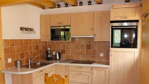 A compact kitchen with wooden cabinets, a built-in oven, and a coffee maker. - Elorian by Interhome (Ovronnaz)