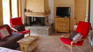 A cozy living room with a stone fireplace, wooden walls, and a television on a wooden cabinet. - Elorian by Interhome (Ovronnaz)
