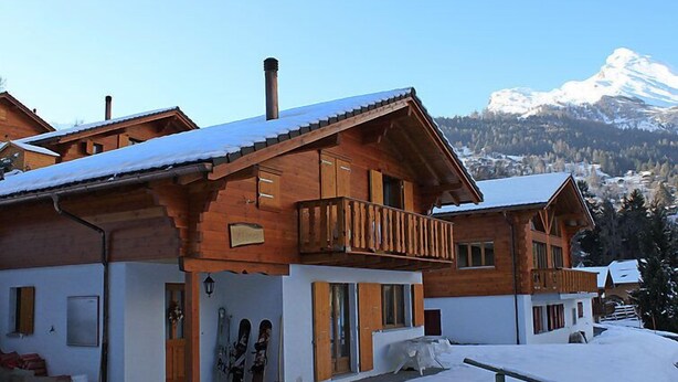 A wooden chalet with a balcony, a snow-covered roof, and a mountain backdrop. - Elorian by Interhome (Ovronnaz)