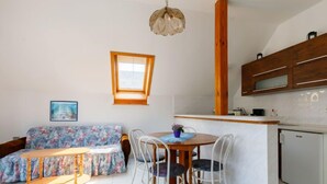 Un espai vital reduït amb sofà, taula de dinar, cadires, petita cuina i una finestra.