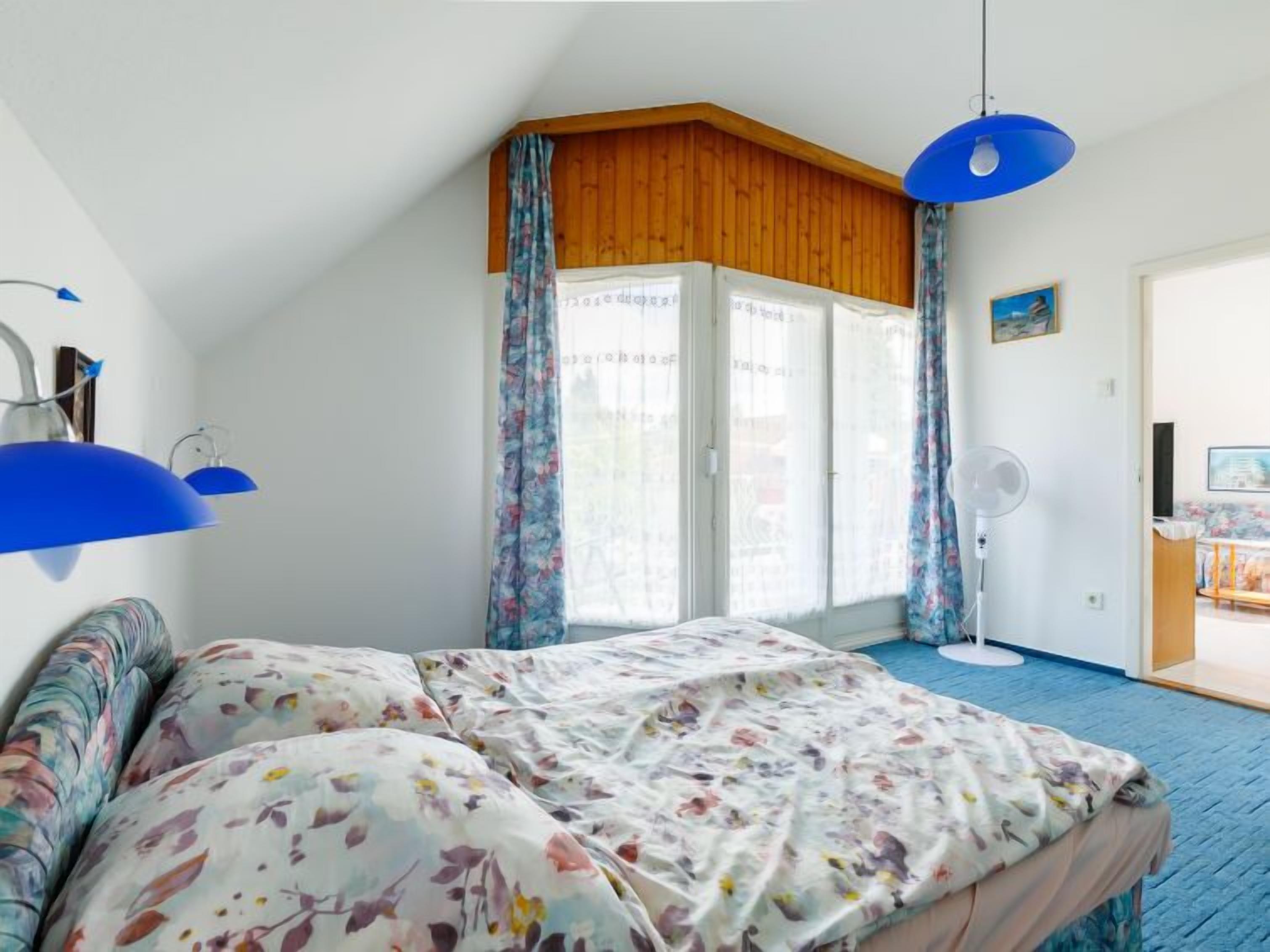 A bedroom with a bed, a fan, and a window with curtains.
