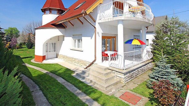 Una casa amb teulada vermella, parets blanques i un balcó amb barana blanca.