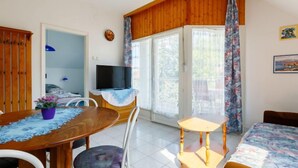Habitació acollidora amb una taula de menjador de fusta, un televisor sobre un moble de fusta, un llit amb un edredó floral i vistes a vegetació a l'exterior.