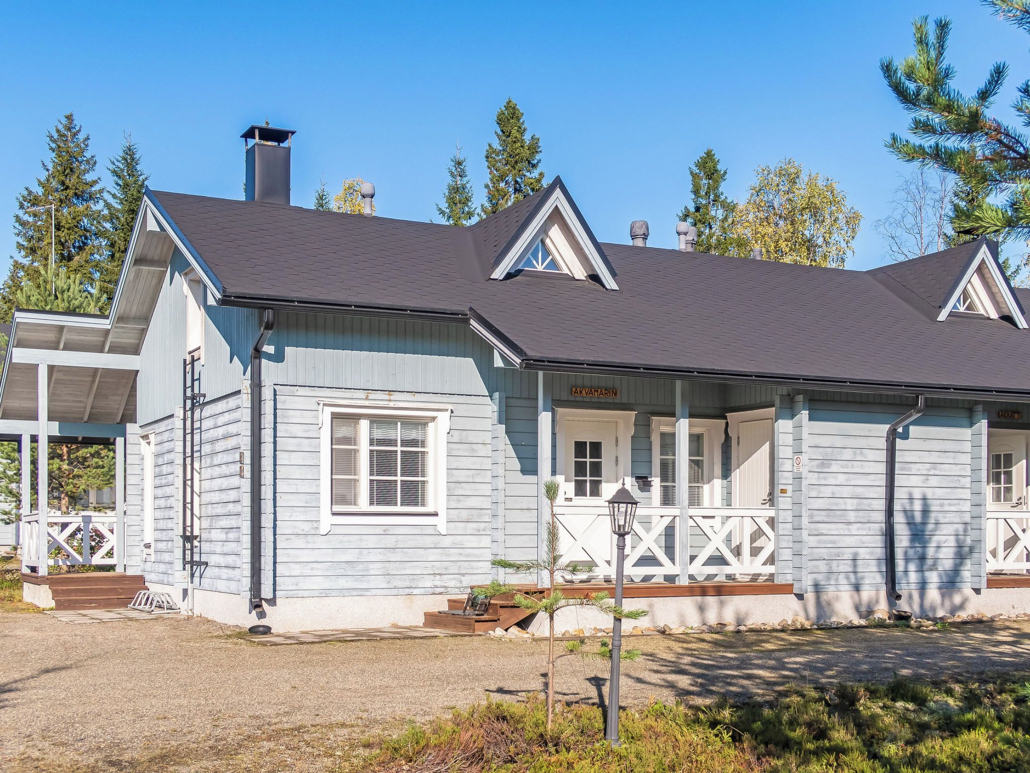 A two-story wooden house with a porch, a chimney, and a small garden area.