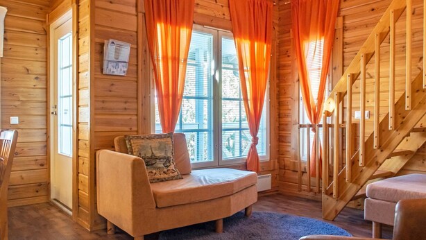 Interior acogedor de una cabaña con paredes de madera, un sofá con un cojín, una pequeña mesa y una escalera.
