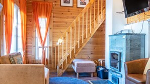 Un interior de madera con una escalera, una chimenea y un televisor montado en la pared.