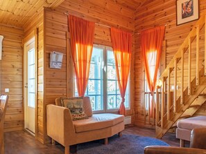Interior acogedor de una cabaña, con detalles de madera, un sofá, una escalera y una ventana con cortinas.