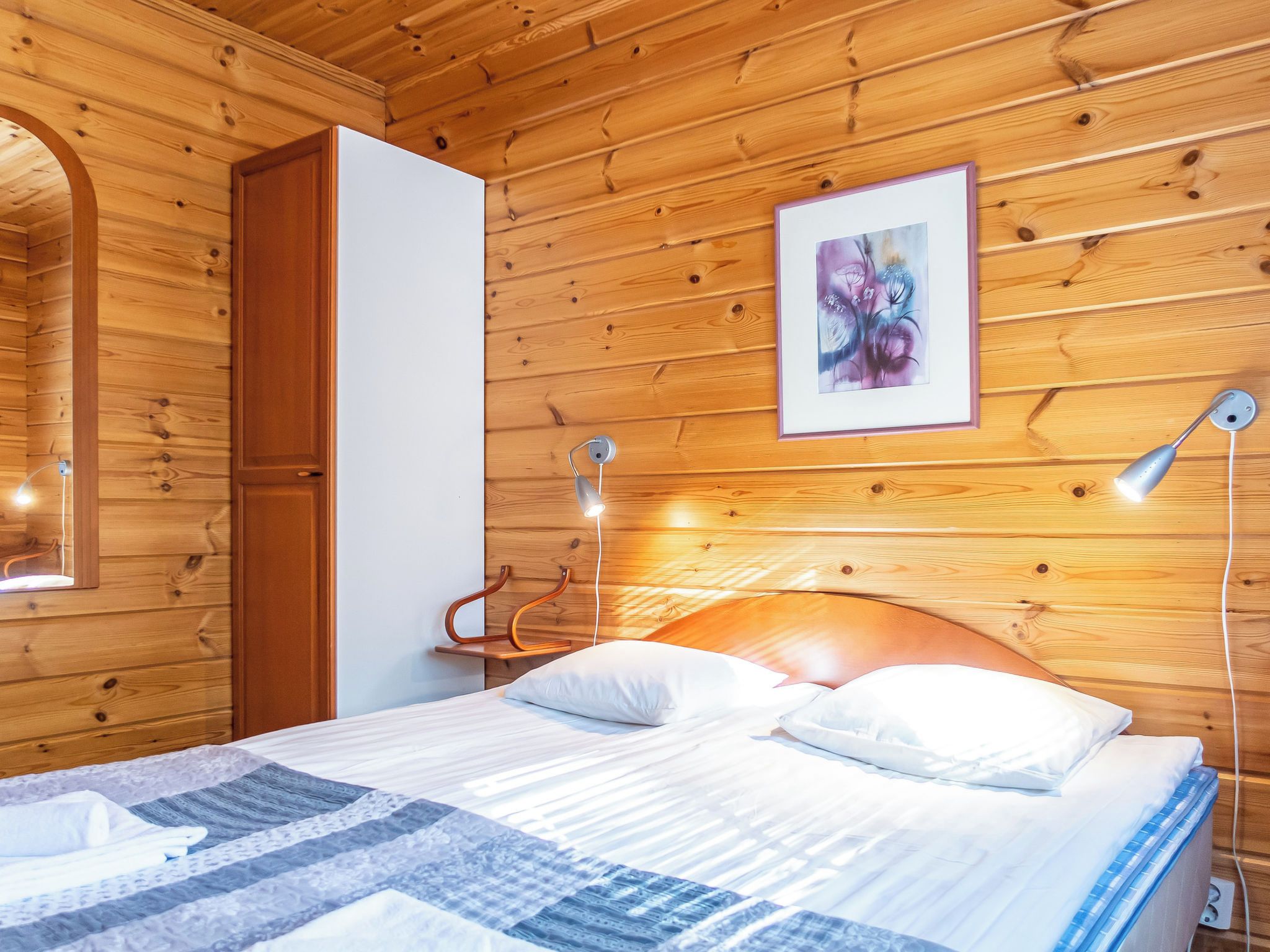 Een kamer met houten lambrisering, een bed, een lijst met een abstract schilderij en een bedlampje.