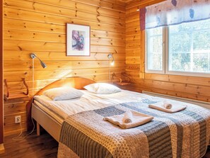 A wooden cabin room with a bed, two bedside lamps, a window with blinds, and a framed picture on the wall.
