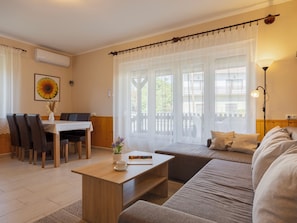 Un salon comprenant un canapé, une table basse, une table à manger avec des chaises et une fenêtre ornée de rideaux légers.