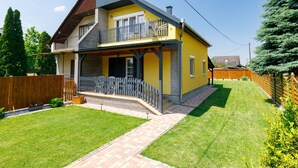 Een huis met twee verdiepingen, een balkon, een houten omheining en een verzorgd gazon.