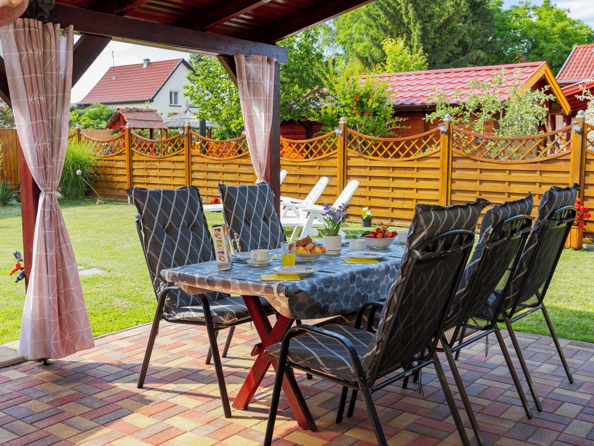 Une terrasse extérieure avec une table dressée pour quatre personnes, entourée de chaises, et une clôture en bois en arrière-plan.