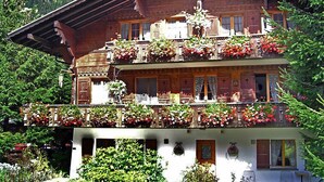 Un chalet de madera tradicional con dos balcones, cada uno decorado con macetas de flores y rodeado de exuberante vegetación.