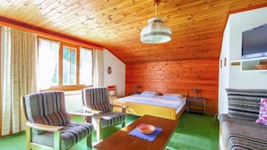 Una habitación acogedora con techo de madera, una cama, dos sillones, una mesa con un bol y un televisor sobre un mueble blanco.