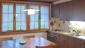 Una cocina con una mesa y sillas de madera, estufa, lavaplatos y una ventana con cortinas.