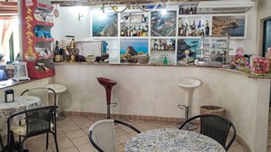 Een bar met verschillende tafels en stoelen, een toonbank met diverse flessen en hapjes, en wanddecoraties waaronder ingelijste foto's.