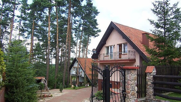 A two-story house with a stone wall and a metal gate, surrounded by tall trees. - Mielno 2 by Interhome (Grunwald)
