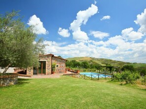 A stone building with a pool, surrounded by a grassy yard and hills in the background.