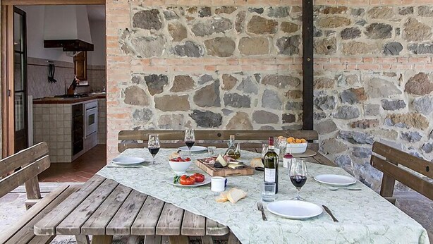 An outdoor dining area with a stone wall backdrop, wooden benches, and a table set for a meal. - Val d'Orcia by Interhome (Radicofani)