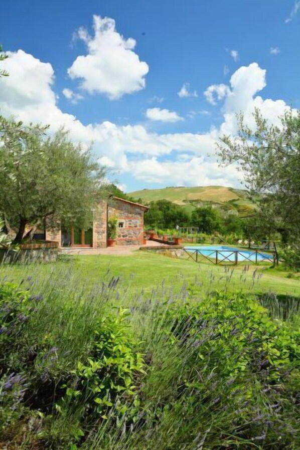 A stone building with a pool, surrounded by lush greenery and hills.