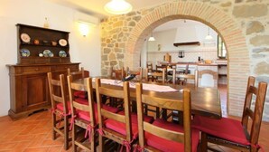 A dining area with a stone archway, wooden chairs with red cushions, a wooden table, and a kitchen visible through the archway. - Val d'Orcia by Interhome (Radicofani)