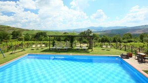 A swimming pool with a checkered pattern, surrounded by a grassy area with lounge chairs and a pergola. - Val d'Orcia by Interhome (Radicofani)