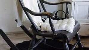 Un fauteuil à bascule noir, agrémenté d’un coussin blanc et d’une serviette blanche drapée sur le dossier.