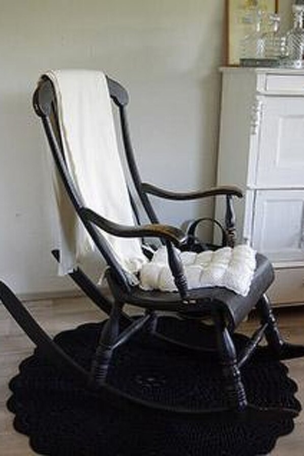 A black rocking chair with a white cushion and a white towel draped over the backrest.