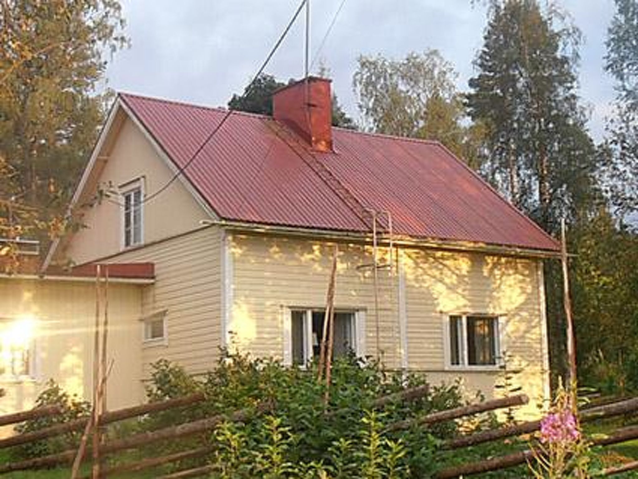 Ett envåningshus med ett rött tak, omgivet av grönska och ett trästaket.