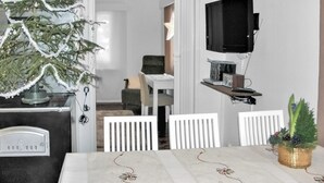 A dining area with a white table, chairs, a Christmas tree, a TV mounted on the wall, and a small plant on the table.