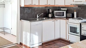 A compact kitchen with a dishwasher, microwave, toaster, and stove. - Villa paasirinne b by Interhome (Toivakka)