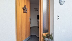 A wooden door with a decorative metal piece, a frosted glass panel, and a potted plant with pine cones on the ground. - Chalet am Reeti by Interhome (Grindelwald)