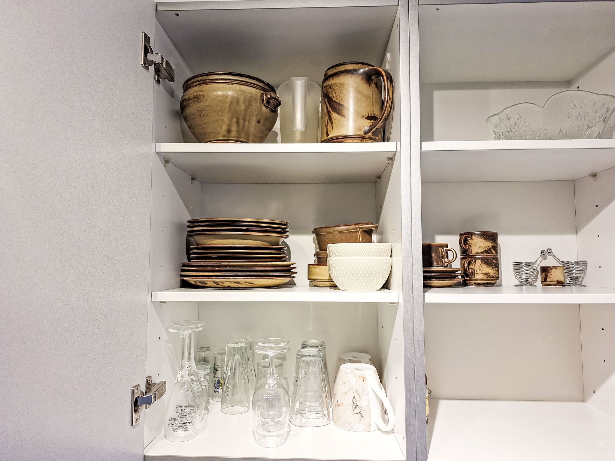 Un meuble blanc, doté d’étagères où sont rangés divers ustensiles de cuisine, notamment des assiettes, des bols et de la vaisselle.