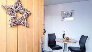 A room with a wooden door, a star decoration, a framed picture on the wall, a round table with two black chairs, and a bottle of wine. - Chalet am Reeti by Interhome (Grindelwald)