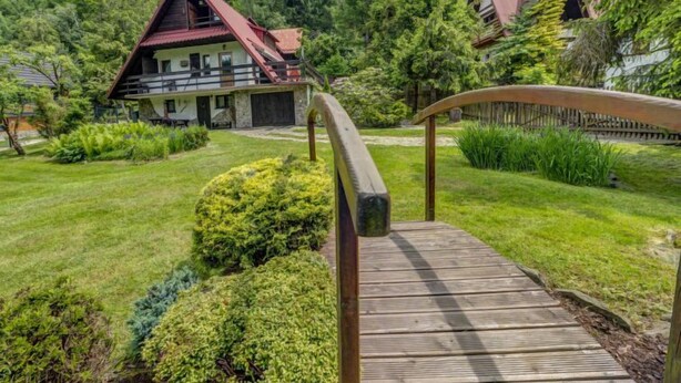 A wooden bridge leading to a chalet with a red roof, surrounded by lush greenery and trees. - Vacation home Hatale by Interhome (Rzyki)