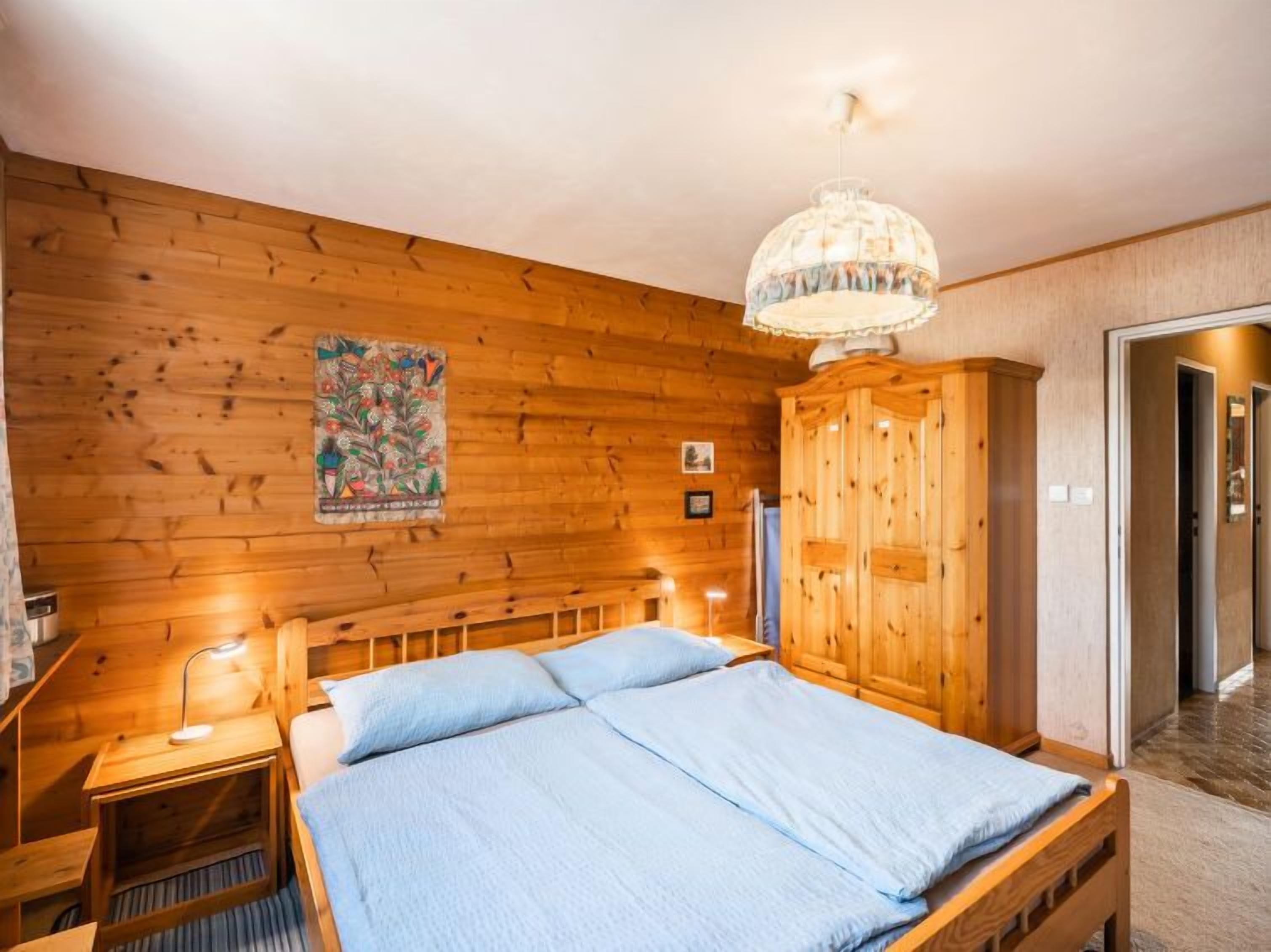 A wooden room with a bed, a nightstand, a wardrobe, and a hanging light fixture.