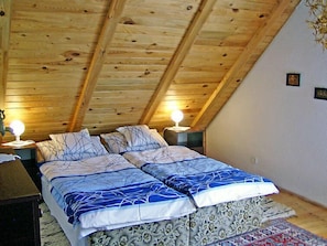 Ein Schlafzimmer mit schrägverdeckter Decke, zwei Nachttische mit Lampen, einem Bett mit gemusterten Betttextilien und einem floralen Teppich.