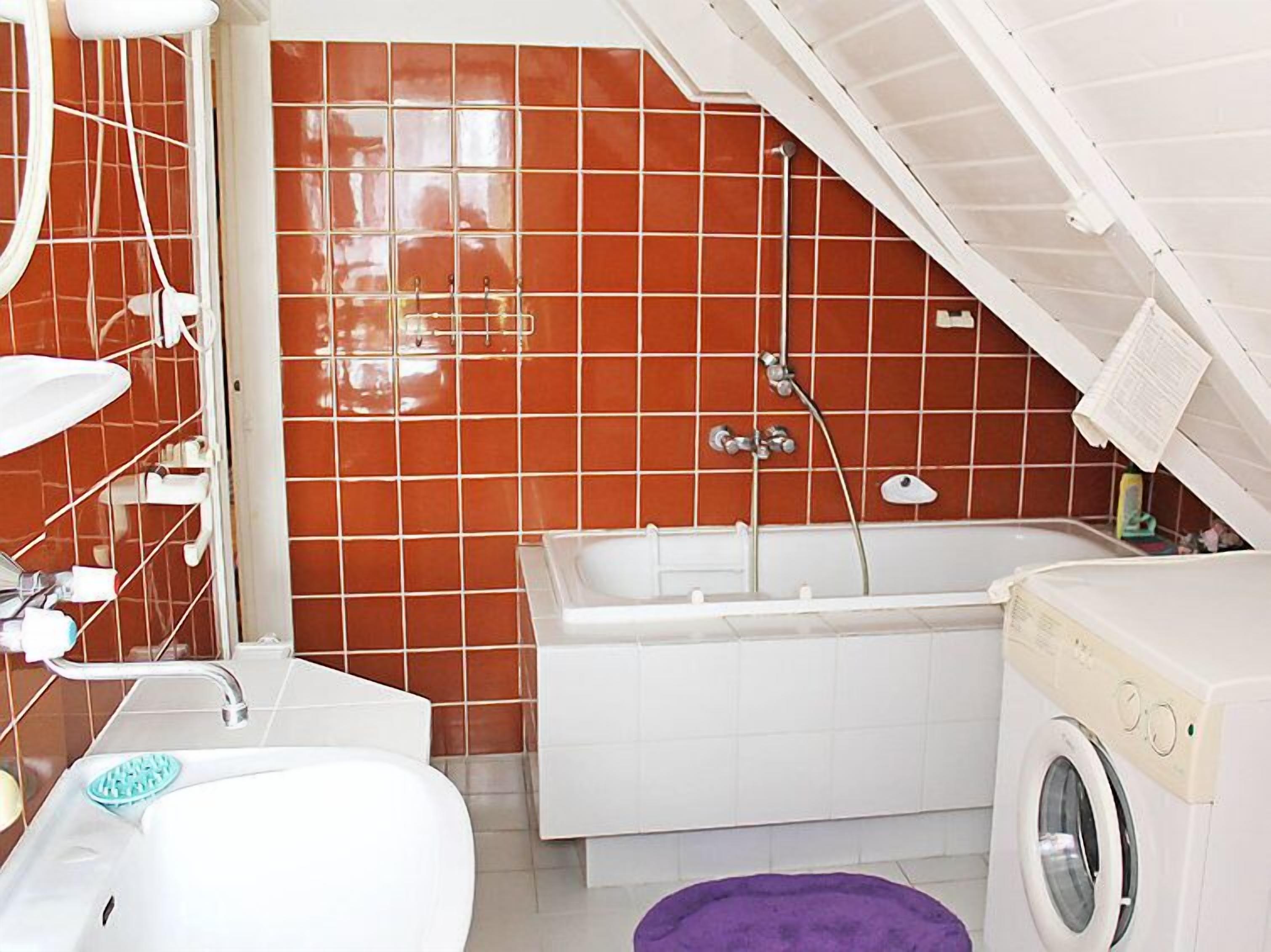Un baño con una bañera blanca, una lavadora y un muro con azulejos.
