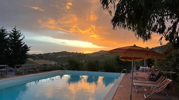 Ein Swimmingpool mit Sonnenuntergangsblick, Liegestühlen und einem Sonnenschirm.