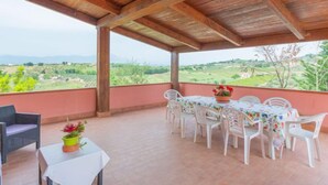 Un porche cubierto con una mesa, sillas, una planta en maceta y vistas al campo.