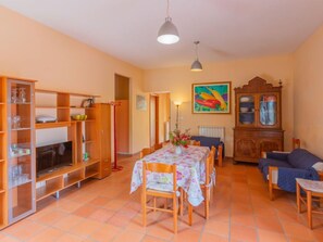 Un salon chaleureux avec un coin repas, des meubles en bois, un téléviseur et un tableau coloré accroché au mur.