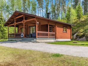 A wooden cabin with a porch, a chimney, and a gravel driveway.