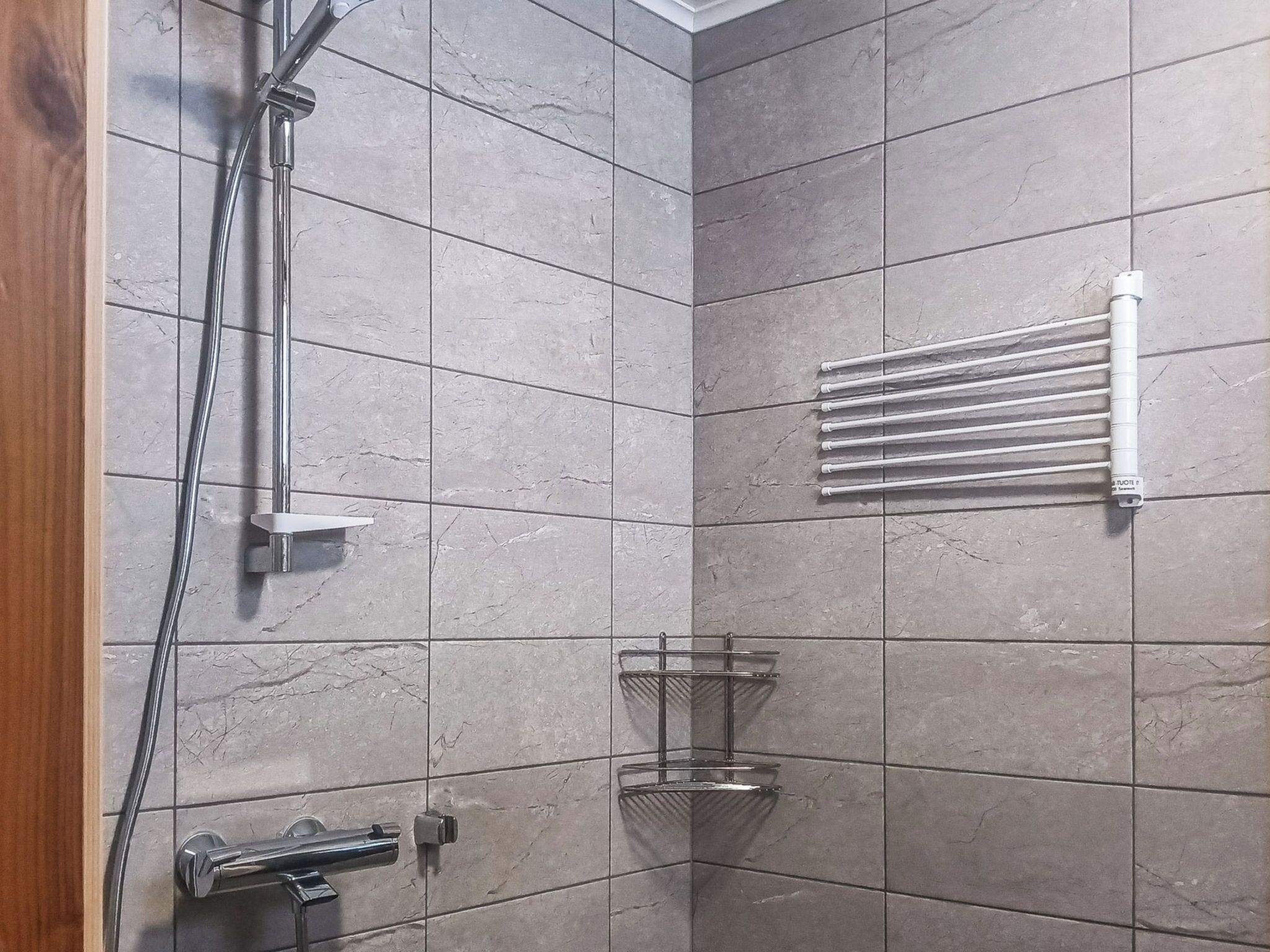 A modern shower area with a handheld showerhead, a wall-mounted towel rack, and a corner shelf.