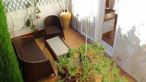 Une terrasse avec des meubles en osier, une petite table et des plantes en pot.