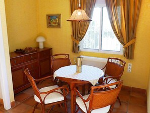A dining area with a round wooden table, four chairs, a chessboard, and a lamp.